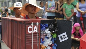 Filipino environmental activists wear a mock container vans filled with garbage to symbolize the 50 containers of waste that were shipped from Canada to the Philippines two years ago as they hold a protest outside the Canadian Embassy in the financial dis