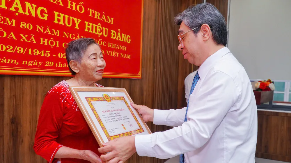 Đồng chí Nguyễn Phước Lộc, Phó Bí thư Thành ủy, Chủ tịch UBMTTQ Việt Nam TPHCM trao Huy hiệu 60 năm tuổi Đảng và tặng hoa chúc mừng đảng viên Dương Thị Xoan (xã Hồ Tràm)