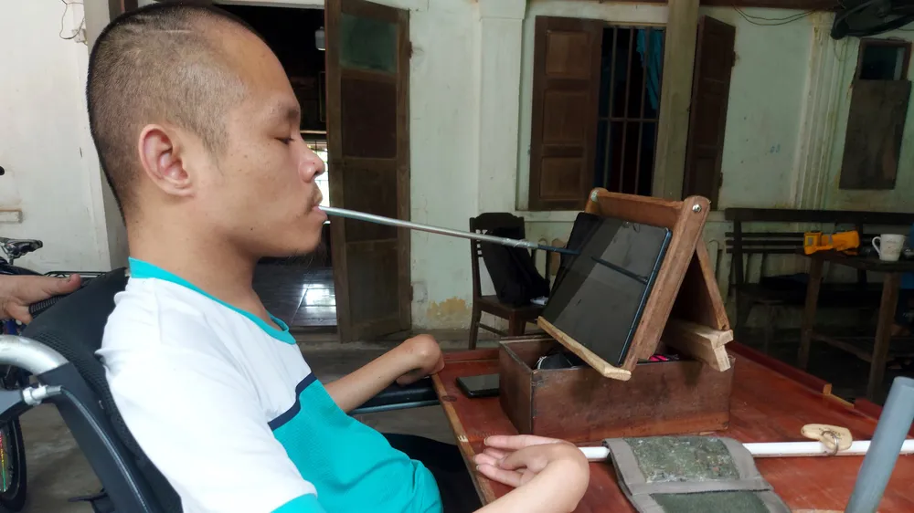 Anh Phạm Sỹ Long ngồi xe lăn ngậm bút tự chế viết truyện trên máy tính bảng