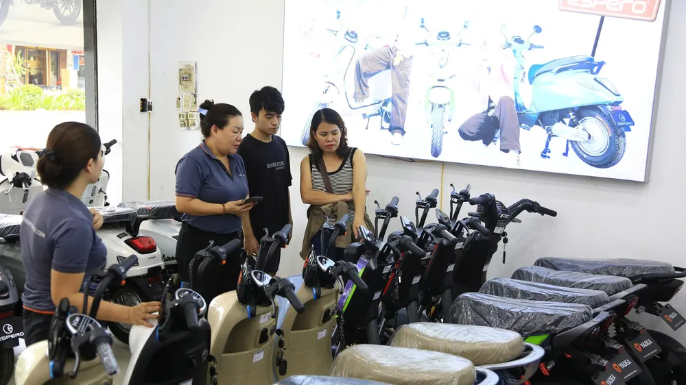 Chị Thu Phương (bìa phải) chọn mua xe máy điện cho con đi học tại một cửa hàng ở Xã Đàn (Hà Nội)