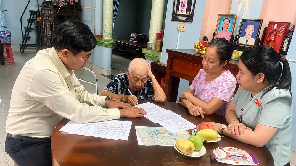Công chức Trung tâm Phục vụ hành chính công xã Hóc Môn hỗ trợ cụ Lê Thị Tỷ thực hiện thủ tục hành chính tại nhà. Ảnh: HỮU TÂM
