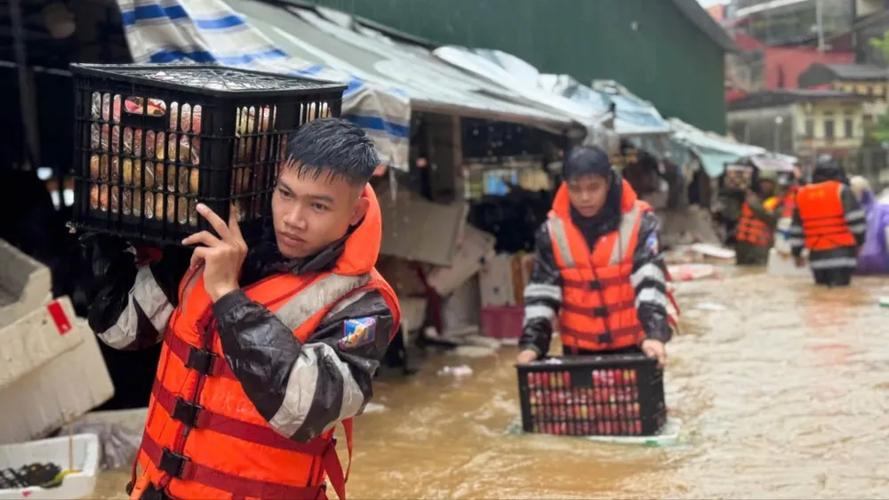 Cảnh sát cơ động cùng các lực lượng chức năng hỗ trợ tiểu thương chợ Giếng Vuông di chuyển hàng hóa khỏi khu vực ngập sáng 22-8. Ảnh: T.N.L.S
