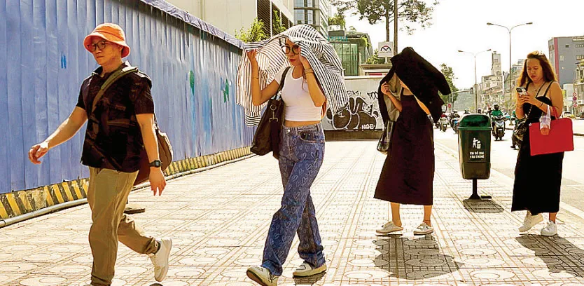 Khách du lịch vừa đi vừa né nắng trên đường Nguyễn Huệ, TPHCM chiều 5-12. Ảnh: HOÀNG HÙNG