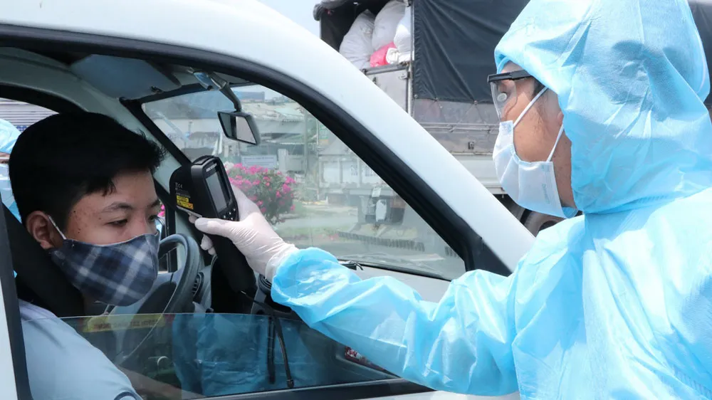 Tổ phòng dịch Covid-19 đo thân nhiệt người tham gia giao thông ở cầu Đồng Nai, cửa ngõ vào TPHCM. Ảnh: PHẠM MINH 