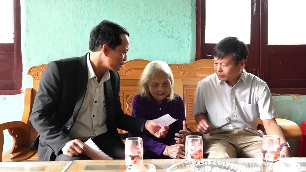 Ông Võ Trung Mạnh (bên trái), Bí thư Đảng ủy, Chủ tịch Ủy ban bầu cử xã Tu Mơ Rông, và ông Trần Quốc Huy (bên phải), Chủ tịch UBND xã, thăm, phát thẻ cử tri cho Mẹ Việt Nam anh hùng Y Tría, đồng thời động viên mẹ yên tâm chăm sóc sức khỏe