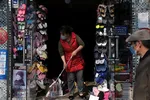 A woman wearing a face mask cleans the entrance of a shop in Beijing on April 17. The coronavirus outbreak has hit China's domestic demand hard. © Reuters