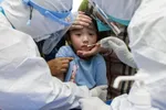 Một đứa trẻ phản ứng với miếng gạc ngoáy họng trong quy trình xét nghiệm hàng loạt tại Vũ Hán, Trung Quốc. Nguồn ảnh: APNews.