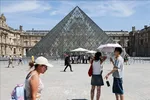 Du khách che ô chống nắng khi tham quan viện bảo tàng Louvre ở Paris, Pháp ngày 25-6. Ảnh: THX/TTXVN