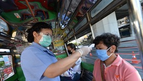 A health worker examines a person's body temperature at a checkpoint in Bangkok, Thailand, on March 26 (Photo: Xinhua/VNA)