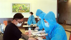 Nhân viên y tế hướng dẫn chuyên gia, lao động nước ngoài khai báo y tế và kiểm tra sức khỏe trước khi vào khách sạn cách ly. (Ảnh: TTXVN)