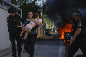 Cảnh sát đưa một phụ nữ bế con chạy ra khỏi khu vực bị tấn công bằng rocket ở Dải Gaza ngày 7-10. (Nguồn: AP)