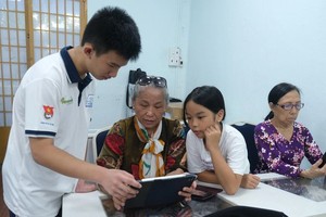 天资高中学校十年级学生晋勇正在指引杨氏蓉老大娘与其孙女使用智能手机、平板电脑上的应用程式。