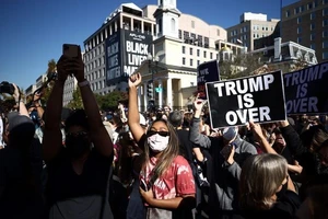 Một số người mang theo cờ Mỹ bà biển hiệu: "Trump đã kết thúc". Nguồn: REUTERS
