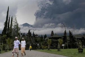 Người dân Bali đi bộ tại đền Besakih ở Karangasem, Bali, Indonesia, phía sau là núi lửa Agung phun trào, ngày 26-11-2017. Ảnh: REUTERS