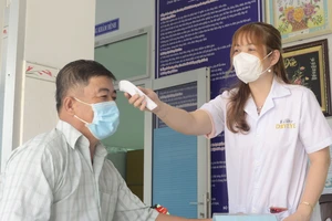 Chị Hồng Gấm đo thân nhiệt cho người dân đến khám chữa bệnh tại Trạm y tế xã An Ngãi Trung