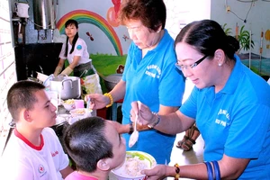 Chị Phạm Ngọc Dung (bìa phải) đến thăm, tặng quà, chăm sóc trẻ em tại Trung tâm Bảo trợ trẻ tàn tật, mồ côi Thị Nghè (TPHCM). Ảnh: MINH THANH
