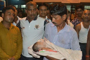 Một người đàn ông bế một trẻ nhi đã tử vong ở bên ngoài Bệnh viên Cao đẳng Y khoa Baba Raghav Das. Ảnh: AP