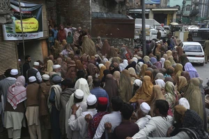 Mọi người chờ đến lượt nhận một bao bột mì miễn phí tại một điểm phân phát ở Peshawar, Pakistan. Ảnh: AP