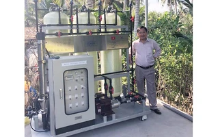 GS Nguyễn Văn Phước và mô hình xử lý nước lắp đặt tại ấp An Quy. Ảnh: IER