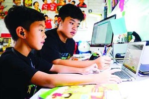 Third-grader Nguyen Huynh Thong is getting used to e-learning with the help of his brother, a seventh grader. (Photo: SGGP)