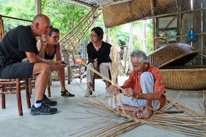 Ông Vũ Văn Khá (làng Kim Bồng, xã Cẩm Kim, TP Hội An) biểu diễn nghề đan thúng chai cho khách nước ngoài thưởng lãm