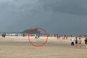 黎謙攝影師(紅圈)正在海灘為一名女遊客拍照時，突然被雷擊中。（圖源:視頻截圖）