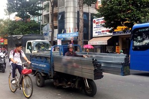 在第十一郡交通密度高的李常傑街上通行的機動三輪車，車上載著特長鐵枝，突出車外的兩頭都沒包住。