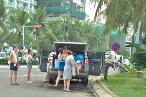 一家約5至7人在峴港海灘路邊停車並當街用淡水沖洗。（圖源：互聯網）