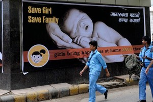 印度男生於2010年7月9日走過新德里的一幅鼓勵女孩誕生的宣傳海報。（圖源：AFP）