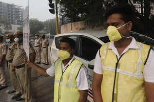 11月4日早晨，志願者和警察戴著防毒口罩站在新德里的十字路口，手舉牌子“服從單雙號限行，消除污染”。（圖源：AP）