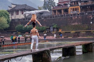 江家兄弟倆在鳳凰古鎮跨河木橋高難度頭頂頭表演一瞥。（圖源：互聯網）