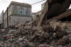 2月14日，在也門首都薩那，當地居民走過一處房屋廢墟。（圖源：新華社）