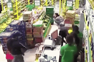 一名手持著疑似手槍的劫匪控制收銀櫃檯員被監控器錄取的畫面。（圖源：視頻截圖）