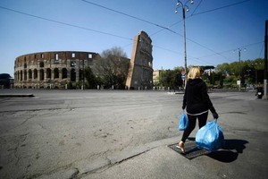 當地時間4月10日，一名婦女背著垃圾袋穿過羅馬體育館紀念碑附近。（圖源：互聯網）