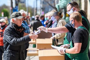 20日，在德國薩克森州首府德累斯頓的市政廳前，工作人員向一名男子發放口罩。（圖源：互聯網）