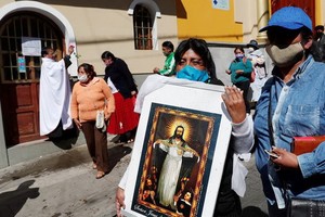 玻利維亞首都拉巴斯的「大能耶穌天主堂」外，信徒們戴口罩，拿著耶穌畫像遊行。（圖源：AP）