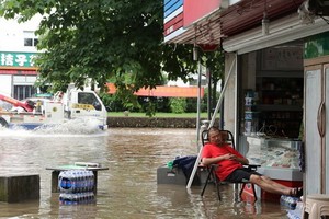 圖為浙江衢州6月30日因大雨導致路面積水，不過當地一名男子仍淡定地在自家雜貨店門口打盹。（圖源：路透社）