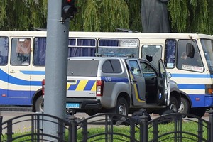 烏克蘭一輛公交車於7月21日在盧茨克市被一名武裝人員劫持，三名執法人員臥倒在公交車旁邊的一輛汽車後面的地上，與歹徒對峙。（圖源：路透社）