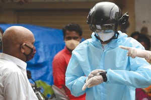 一名非政府組織的衛生工作志願者穿著防護衣，戴著裝有熱掃描傳感器的智能頭盔在居民區挨戶查看居民體溫。（圖源：Getty Images）