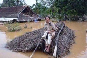 在一片汪洋的洪水之中，一名婦女坐在草屋頂上等待營救。（圖源：互聯網）