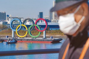 一名戴口罩的男子在奧運五環背景中行走。（圖源：AP）