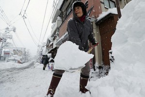 一名女子在日本新潟縣湯澤的街頭鏟雪。（圖源：路透社）
