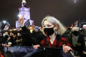 在波蘭首都華沙，數以千計的女性和年輕人當地時間週三晚不顧防疫限制，點燃火炬、揮舞支持性小眾權利的彩虹旗和與手持標語牌，上街抗議墮胎法令。（圖源：路透社）