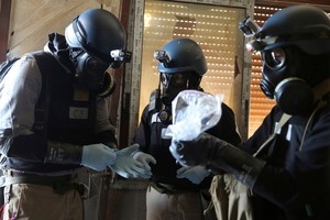 敘利亞危機爆發以來，敘境內的杜馬鎮、薩拉基卜市等多個地點據稱曾發生化武襲擊事件。戴著防毒面具的聯合國化學武器專家檢測一個裝有生化學武器襲擊的樣品。 （圖源：路透社）