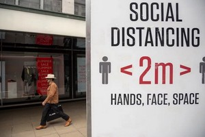 圖為英國倫敦一名男子從提示人們保持社交距離的牌子旁走過。（圖源：新華社）