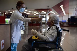 古巴首都哈瓦那何塞·馬蒂國際機場工作人員（左）為入境旅客測量體溫。（圖源：互聯網）