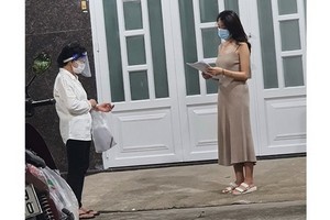 平盛郡第十九坊第三街區第四十六組長黎氏玉貝（左）挨家挨戶派發疫苗接種登記表。