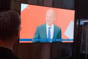 26日晚，在德國萊法州駐柏林代表處內舉辦的選舉之夜活動上，人們在電視前觀看社民黨總理候選人肖爾茨發表演講。（圖源：互聯網）