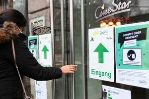 去年12月3日，在德國法蘭克福一家電影院外，一名女子從張貼防疫提示牌的入口處進入。（圖：新華社）