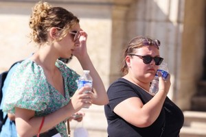 圖為7月13日，在法國巴黎盧浮宮博物館玻璃金字塔廣場上，一名女子把冰鎮礦泉水貼在臉上解暑。（圖：新華社）